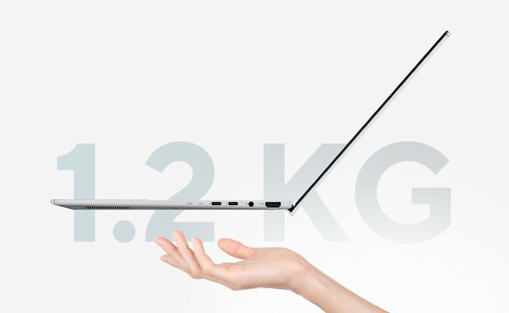 Obraz przedstawia otwarty laptop trzymany nad dłonią, z widocznymi portami na boku. W tle znajduje się duży napis \'1.2 KG\'.