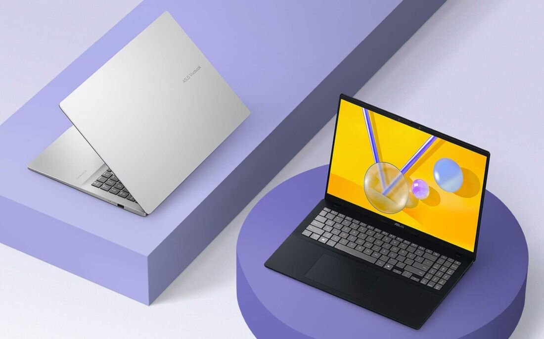 Na obrazie widoczne są dwa laptopy na fioletowych powierzchniach. Jeden z nich jest zamknięty i srebrny, drugi otwarty z widocznym kolorowym ekranem i czarną klawiaturą.