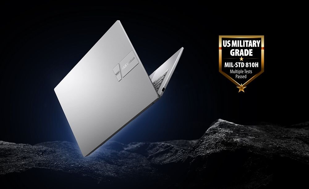 Srebrny laptop z logo ASUS unosi się nad ciemnym, skalistym tłem. Obok widoczna jest odznaka z napisem \'US MILITARY GRADE MIL-STD 810H Multiple Tests Passed\'.