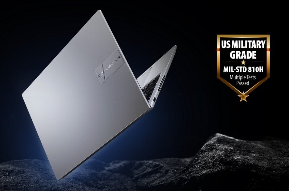 Srebrny laptop z widocznym logo ASUS Vivobook unosi się nad ciemnym tłem. Obok znajduje się odznaka z napisem \'US MILITARY GRADE MIL-STD 810H Multiple Tests Passed\'.