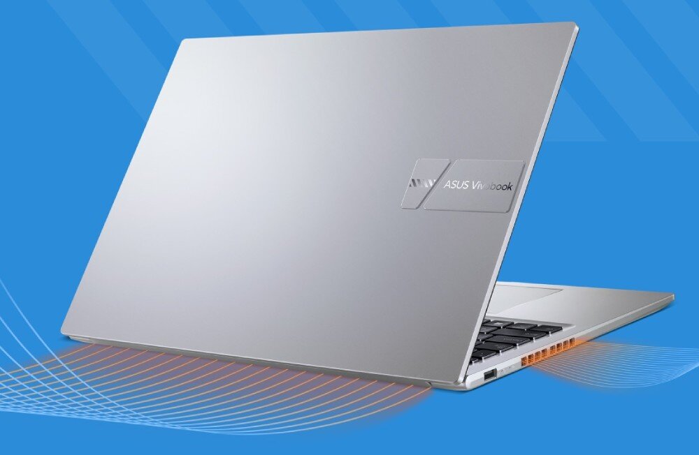 Srebrny laptop z widocznym logo \'ASUS Vivobook\' na pokrywie, ustawiony na niebieskim tle z pomarańczowymi i białymi liniami w dolnej części obrazu.