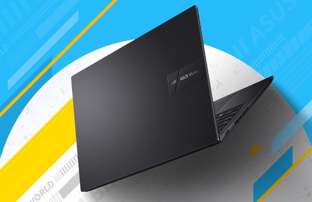 Czarny laptop z widocznym logo \'ASUS Vivobook\' na pokrywie. Tło jest kolorowe, z elementami niebieskimi i żółtymi.