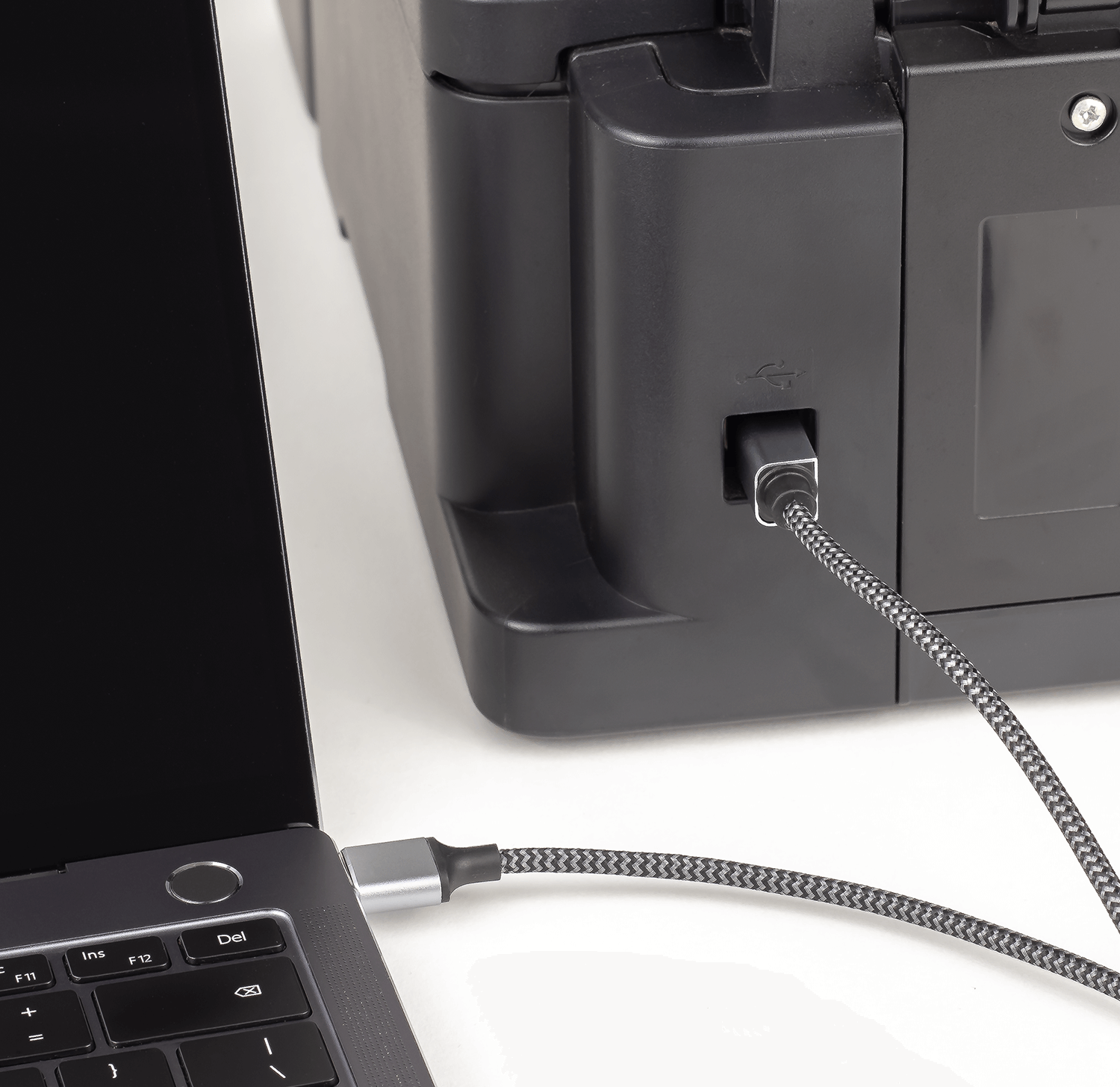 Czarny laptop z podłączonym czarno-srebrnym kablem USB do drukarki. Kabel jest wpięty do portu USB w drukarce.