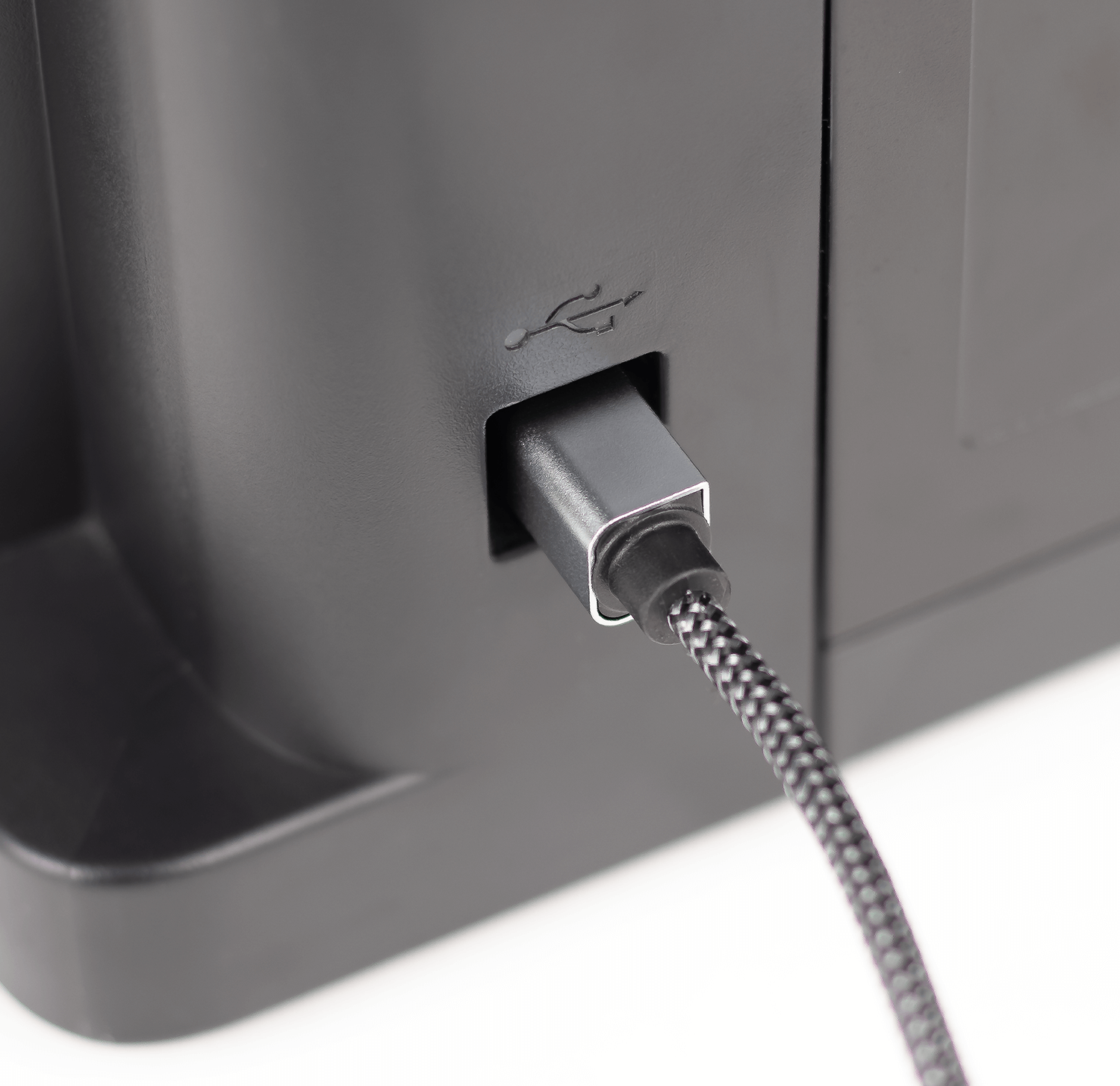 Czarny kabel USB z plecionym oplotem jest podłączony do portu w urządzeniu. Obok portu znajduje się symbol USB.
