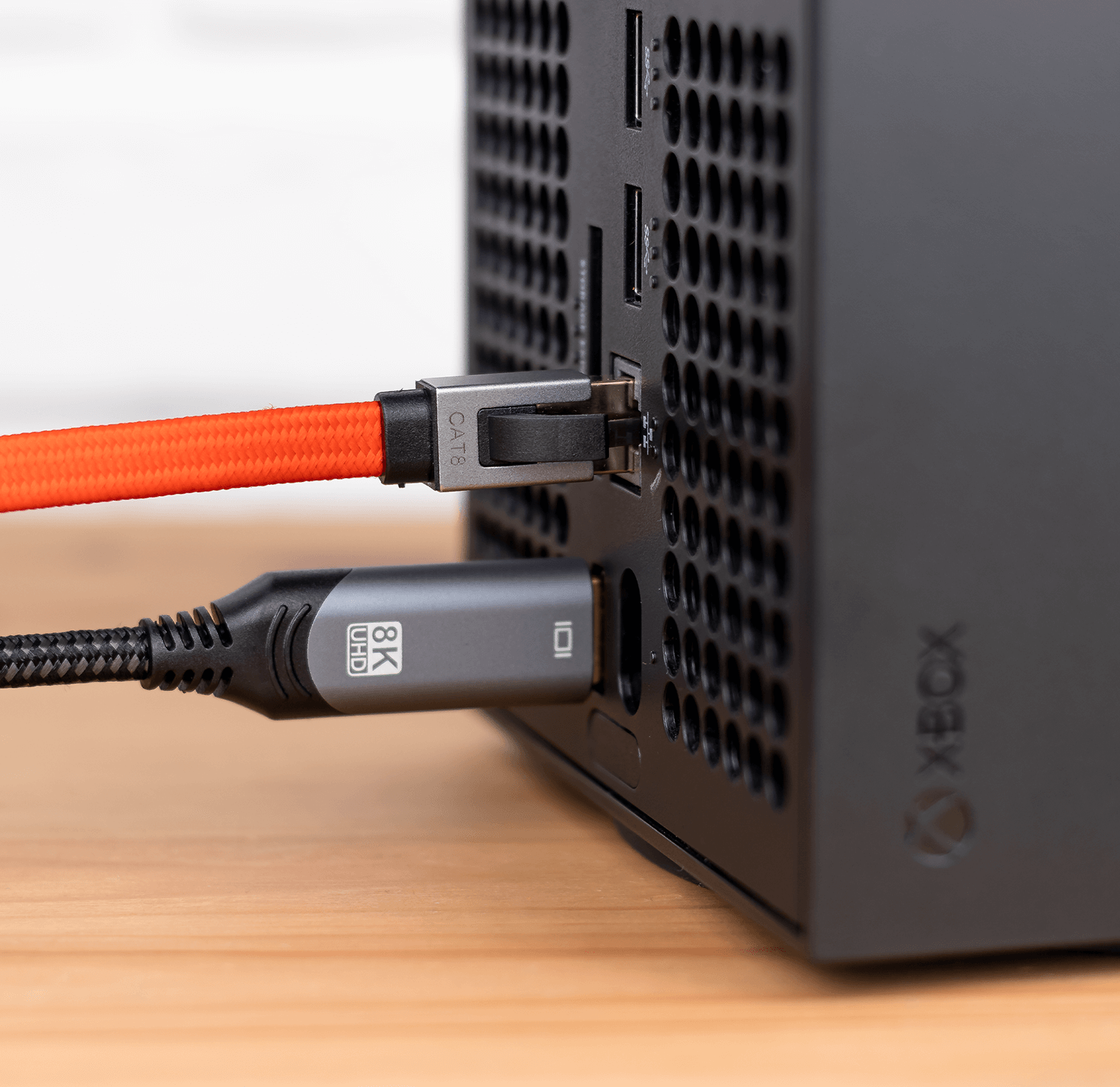 Czerwony kabel sieciowy z oznaczeniem CAT 8 jest podłączony do urządzenia z widocznym logo XBOX. Obok znajduje się czarny kabel z oznaczeniem 8K UHD.