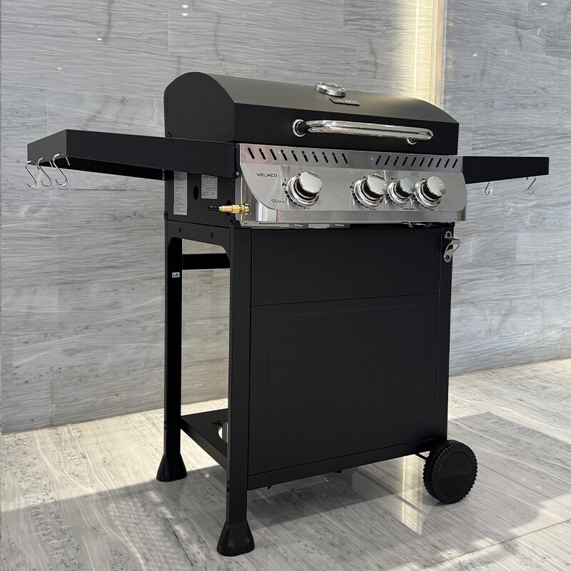 Czarny grill gazowy z czterema pokrętłami i dwoma bocznymi półkami, na jednej z nich znajdują się haczyki. Na przednim panelu widoczne jest logo \'VELACO\'.