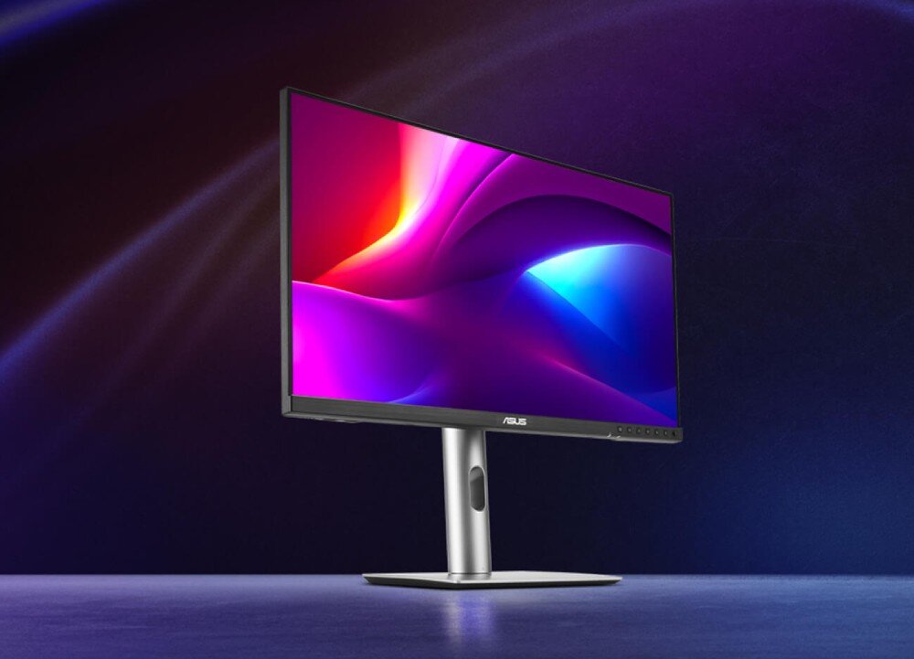 Monitor ASUS ProArt Display PA27JCV Monitor komputerowy z cienkimi ramkami wyświetla kolorową grafikę w odcieniach fioletu, czerwieni i niebieskiego, ustawiony na biurku z jednolitym, ciemnym tłem, opis