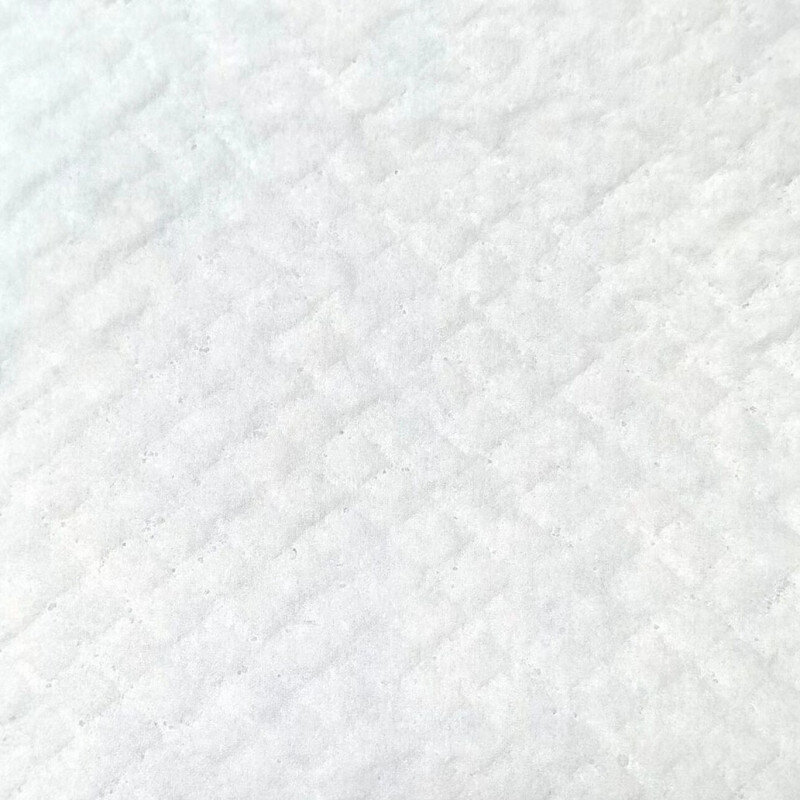 Obraz przedstawia zbliżenie na powierzchnię materiału o teksturze przypominającej pikowanie. Materiał jest w jasnym kolorze, prawdopodobnie białym lub bardzo jasnym różowym.