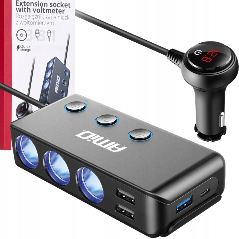 Na obrazie widoczny jest rozgałęziacz gniazda zapalniczki z trzema gniazdami, dwoma portami USB i wyświetlaczem woltomierza. Obok znajduje się opakowanie z napisem \'Extension socket with voltmeter Rozgałęźnik zapalniczki z woltomierzem\'.