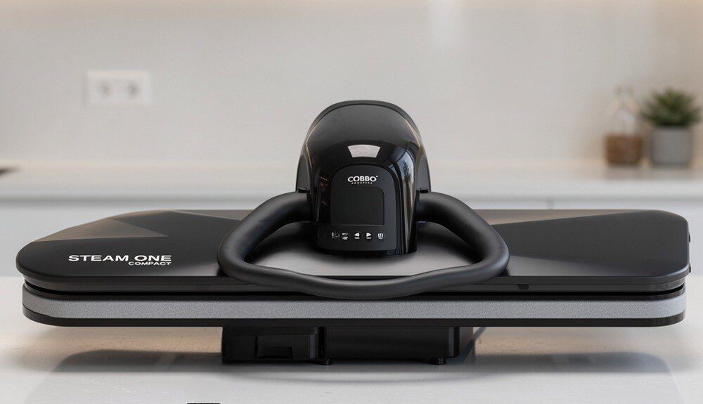 Czarny system do prasowania COBBO Steam One Compact 32 z widocznym logo COBBO na górze urządzenia. Na powierzchni znajduje się napis \'STEAM ONE COMPACT\'.
