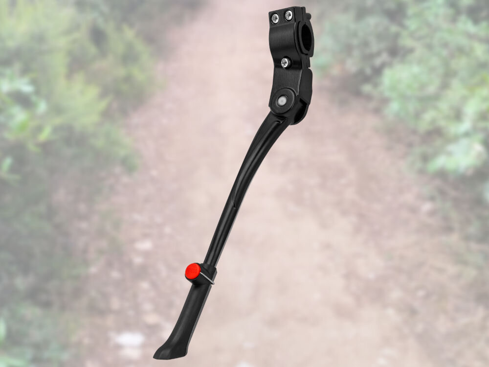 Czarna stopka do roweru z czerwonym elementem, widoczna na tle rozmytej ścieżki w lesie. Stopka ma metalowe mocowanie z dwoma śrubami.