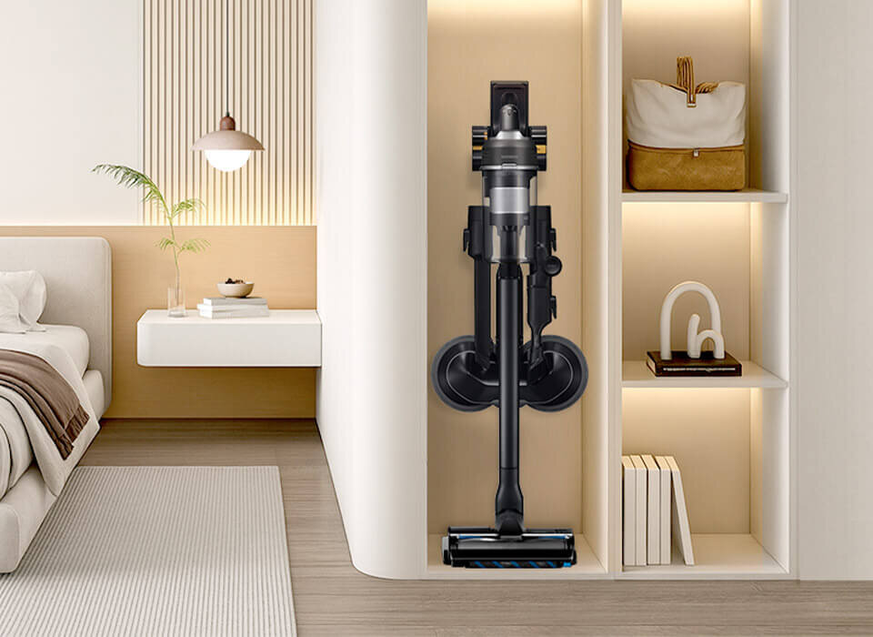 Wnętrze nowoczesnego pokoju z odkurzaczem stojącym w wnęce regału. Obok znajduje się biurko z lampą, rośliną i książkami.