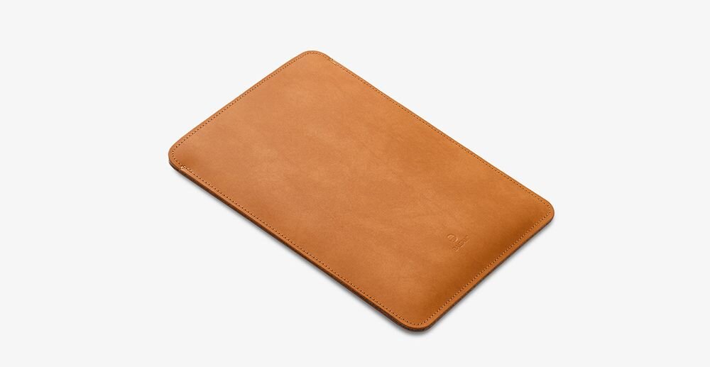 Jasnobrązowe etui na laptopa o prostokątnym kształcie, wykonane z gładkiego materiału. Na powierzchni widoczne jest subtelne logo producenta.