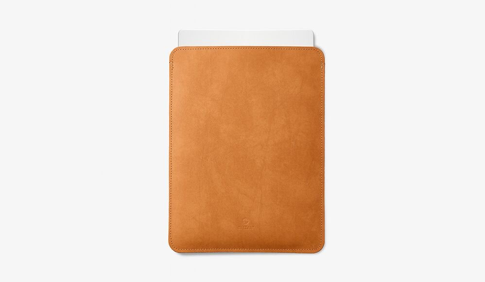 Jasnobrązowe etui na laptopa z widocznym logo producenta na dole. Wystaje z niego biały element, prawdopodobnie część laptopa.