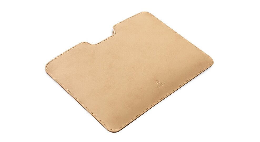 Beżowe etui na laptopa o prostokątnym kształcie z zaokrąglonymi rogami i wycięciem na środku jednej z krawędzi. Na powierzchni widoczne jest wytłoczone logo producenta.