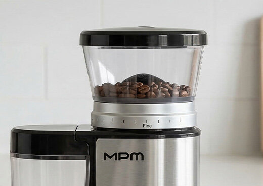 Zbliżenie na młynek stożkowy MMK-09M, w którym znajdują się ziarna kawy.