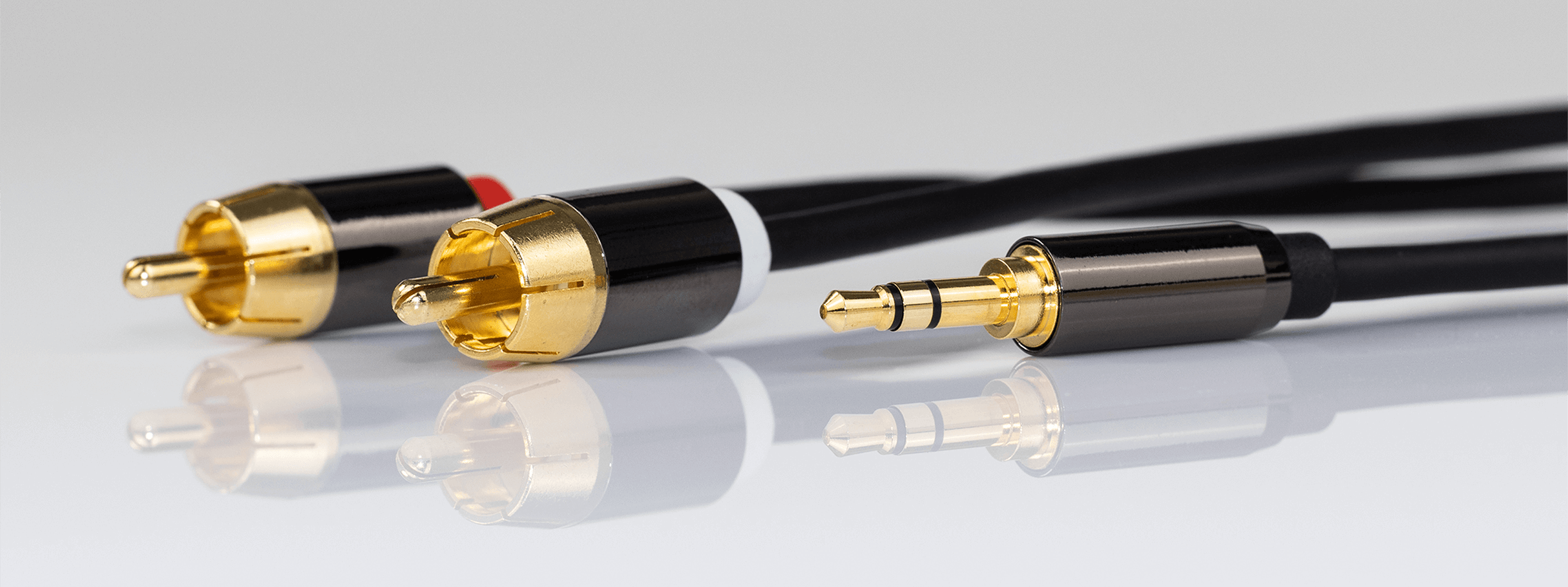 Na obrazie widoczne są trzy końcówki kabli: dwa wtyki RCA z pozłacanymi końcówkami i jeden wtyk Jack 3.5 mm również z pozłacaną końcówką. Kable mają czarne osłony.
