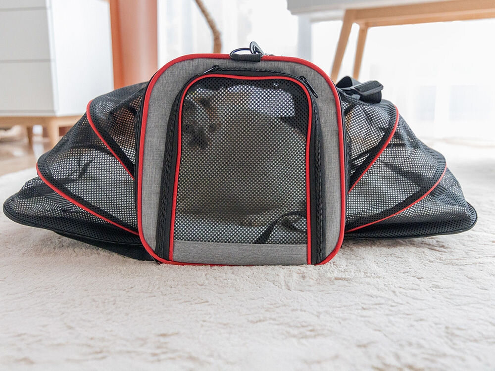 Widok z przodu na szarą torbę transportową z czerwonymi lamówkami i dwoma symetrycznie rozłożonymi bokami z czarnej siatki.