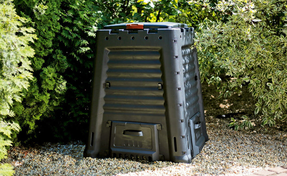 Kompostownik KETER Mega composter 650 l Czarny kompostownik na kamyczkach ustawiony na tle krzewów naturalny nawóz ekologia prosty montaż oszczędność wydajność