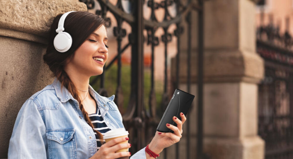 Czytnik e-booków INKBOOK Solaris Color 6 cali, Podświetlany ekran, Wi-Fi Niebieski kobieta trzymająca czytnik stojąca przy murku z założonymi słuchawkami w drugiej ręce kubek czytanie tradycyjne audiobooki Text To Speech zamiana tekstu na mowę