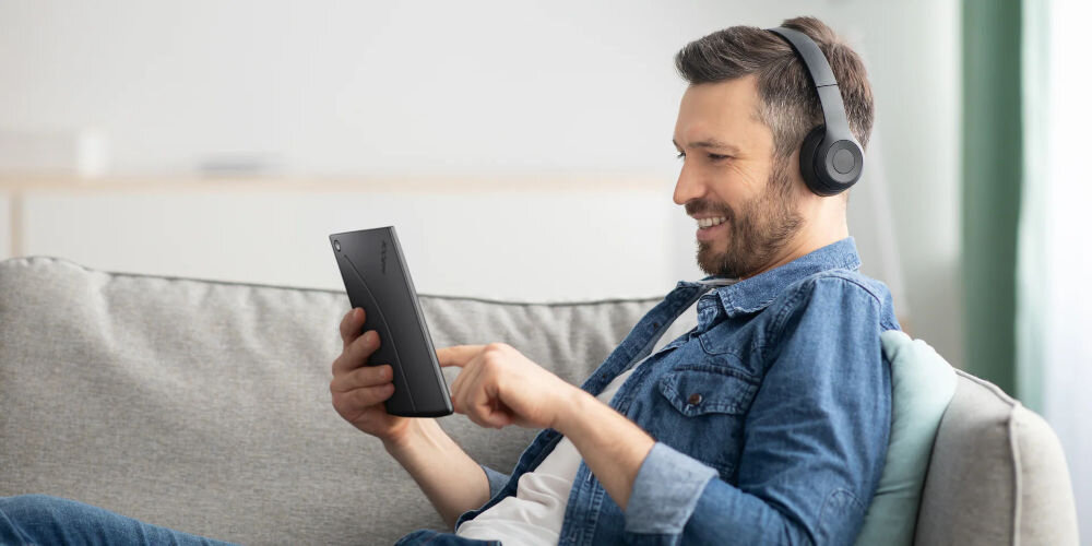 Czytnik e-booków INKBOOK Solaris Color 6 cali, Podświetlany ekran, Wi-Fi Niebieski mężczyzna siedzący na kanapie z czytnikiem i założonymi słuchawkami w pokoju trzy ekrany główne interfejs dotykowy fizyczne przyciski ułatwienie korzystania z czytnika dopasuj sposób nawigacji do preferencji