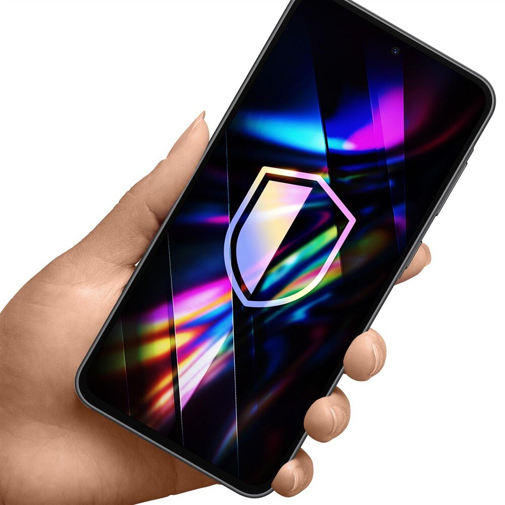 Osoba trzyma smartfon z kolorowym, abstrakcyjnym wzorem na ekranie, na którym widoczny jest symbol tarczy. Ekran telefonu jest błyszczący i odbija światło w różnych kolorach.