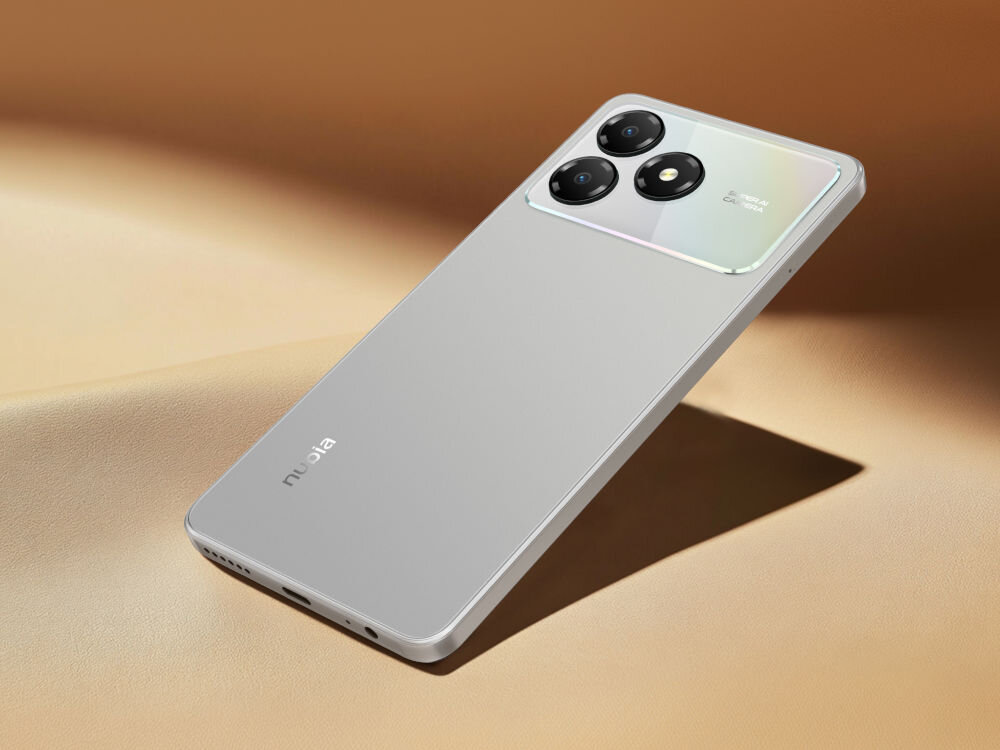 Smartfon ZTE Blade A36 4/64GB 6.75 90Hz Czarny Zbliżenie na tylną część srebrnego telefonu ZTE/nubia z błyszczącą ramką i potrójnym aparatem, na tle brązowej skóry lub zamszu. Widoczny jest port USB-C i głośnik na dole.