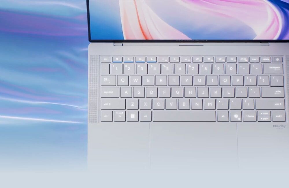 Obraz przedstawia klawiaturę laptopa z podświetleniem, na której widoczne są klawisze z literami i cyframi. W prawym dolnym rogu znajduje się logo \'Dolby\'.