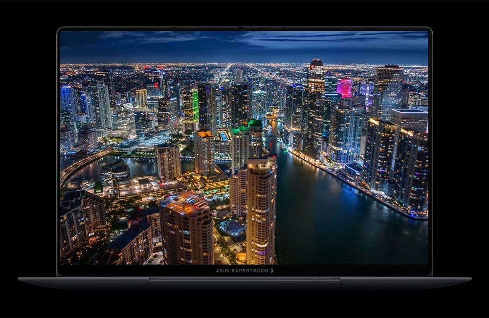 Laptop z wyświetlaczem pokazującym nocną panoramę miasta z oświetlonymi wieżowcami i rzeką. Na dolnej ramce ekranu widoczny jest napis \'ASUS EXPERTBOOK\'.