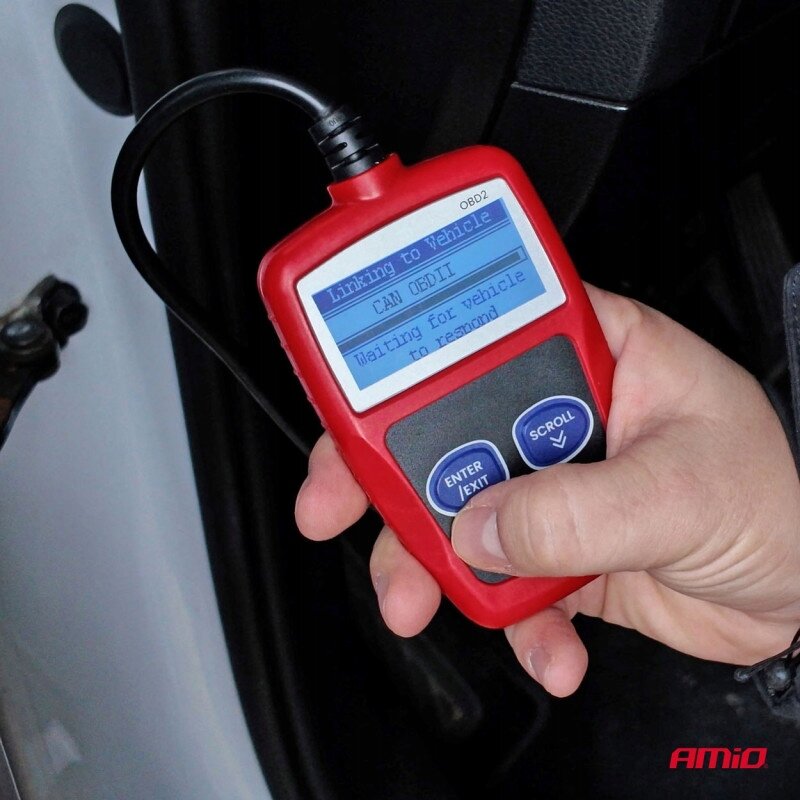 Osoba trzyma czerwony skaner diagnostyczny OBD2 z wyświetlaczem pokazującym tekst: \'Linking to Vehicle CAN OBDII Waiting for vehicle to respond\'. W prawym dolnym rogu widoczne jest logo \'AMiO\'.