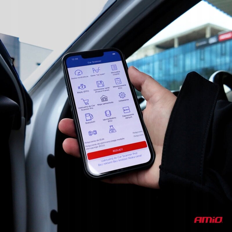 Osoba trzyma smartfon z aplikacją Car Scanner, na ekranie widoczne są ikony i teksty dotyczące funkcji diagnostycznych. W prawym dolnym rogu zdjęcia znajduje się logo \'AMiO\'.