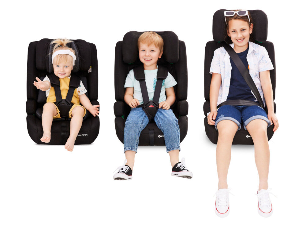 Trzy dzieci siedzą w czarnych fotelikach samochodowych marki Kinderkraft. Foteliki mają widoczne pasy bezpieczeństwa i logo \'kinderkraft\' na dole.