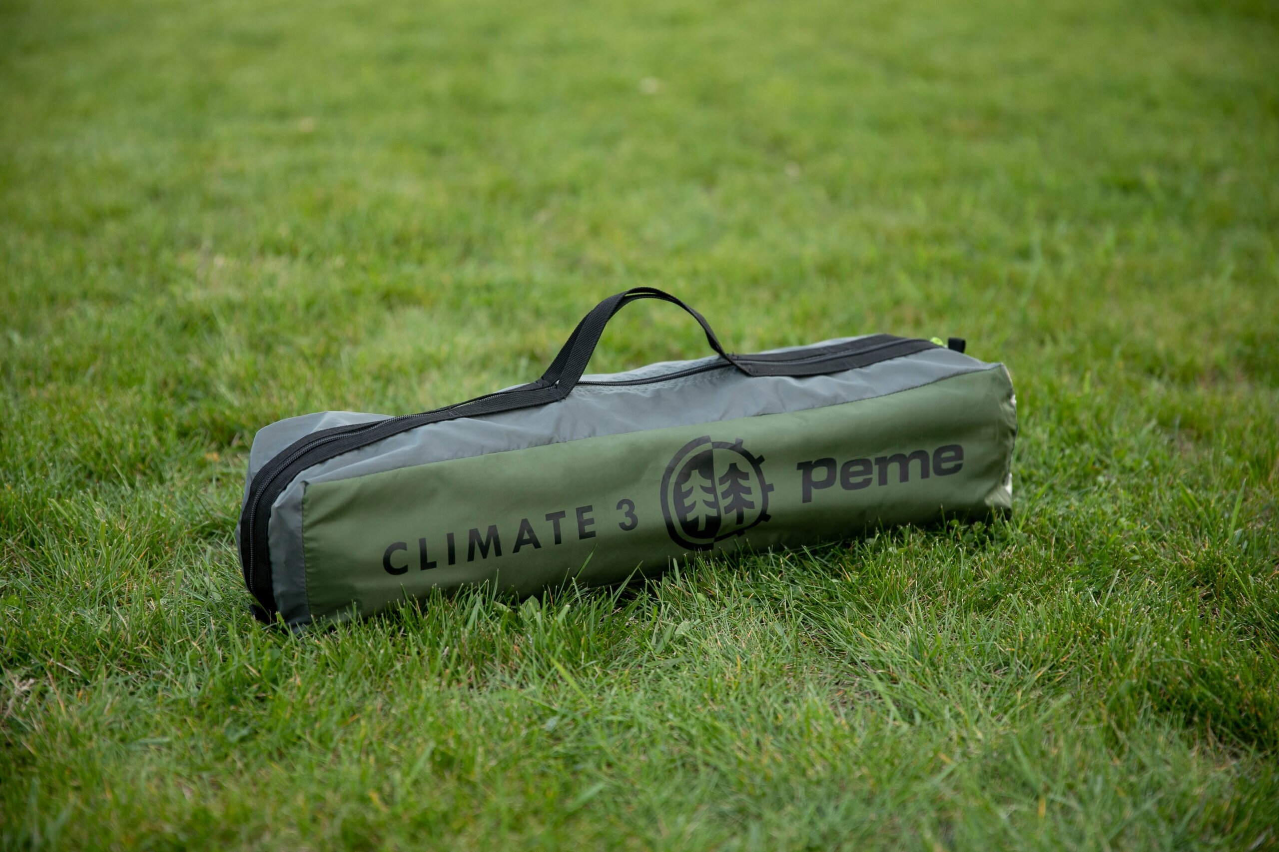 Na trawie leży zielona torba z czarnym uchwytem, na której widnieje napis \'CLIMATE 3\' oraz logo i napis \'peme\'.