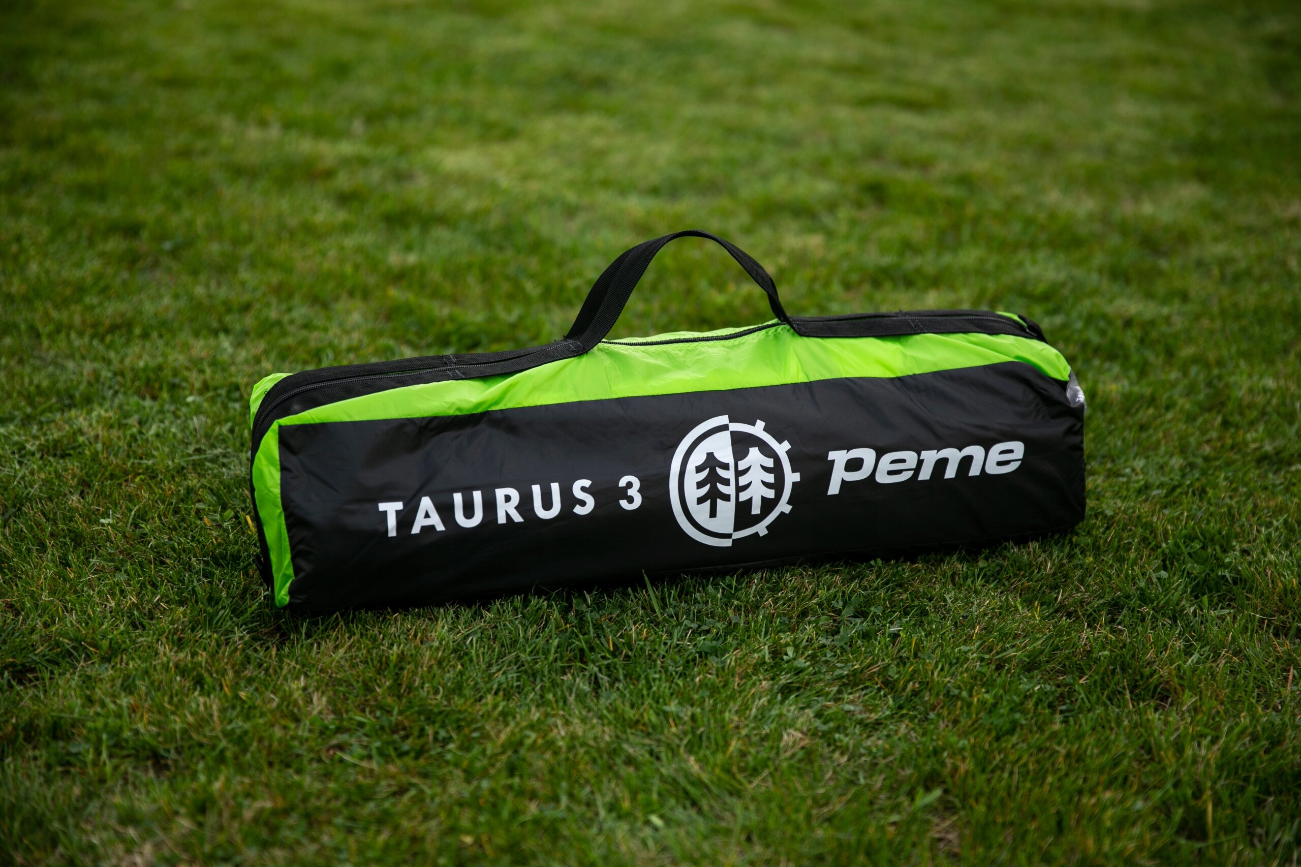 Na trawie leży czarno-zielona torba z napisem \'TAURUS 3\' oraz logo \'peme\'.