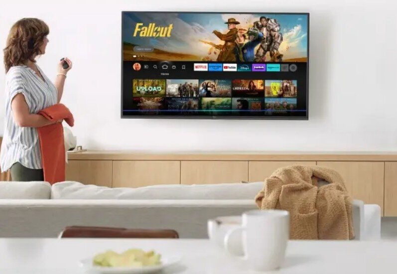 Telewizor PANASONIC TV-50W85BEZ sterowanie głosowe Alexa wygoda funkcji, osoba trzymająca pilota w ręku, telewizor zawszony na ścianie