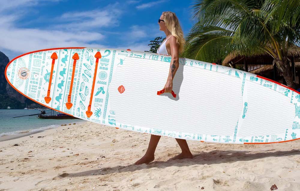 Deska SUP FUNWATER SUPFW05D Zielony, pianka, EVA, przyczepność, joga, Kobieta niesie deskę SUP po piaszczystej plaży.