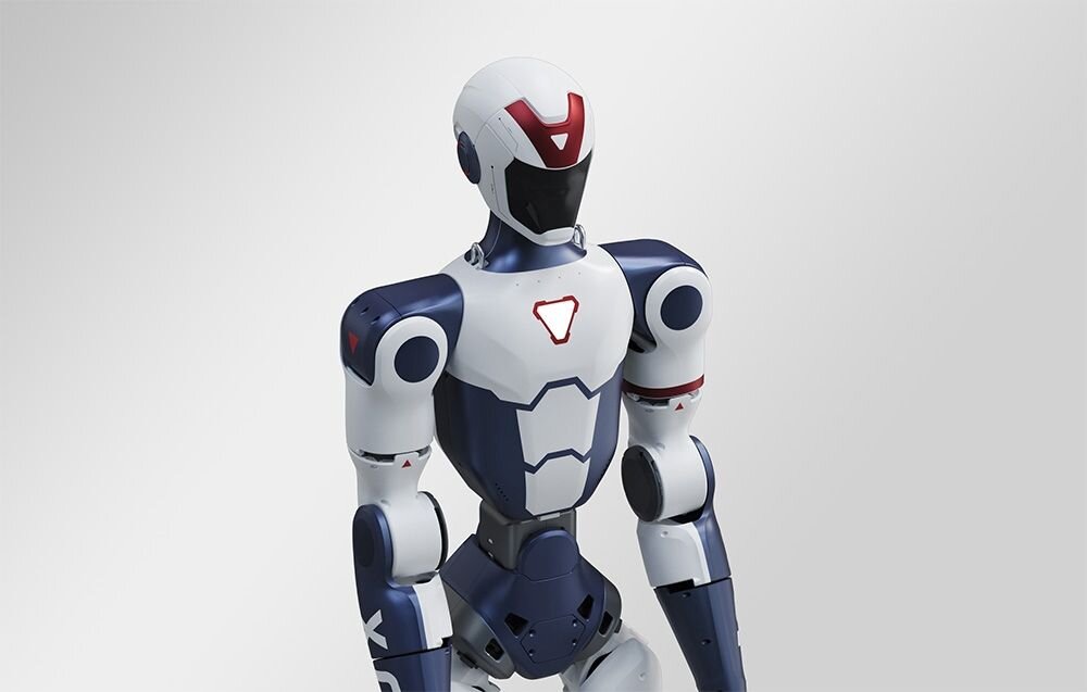 Humanoidalny robot o białej i granatowej kolorystyce z czerwonymi akcentami, z widocznymi elementami przypominającymi pancerz.
