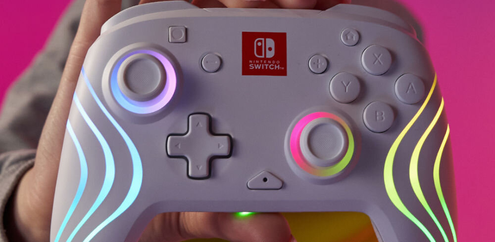 Kontroler PDP Afterglow Wave Nintendo Switch/Nintendo Switch Oled Biały prezentacja kontrolera trzymanego w ręcę na różowym tle