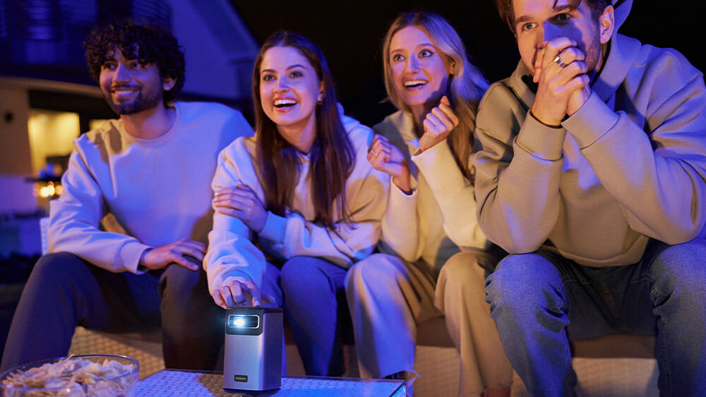 Projektor OVERMAX Multipic 8.1 HD - Wytrzymała lampa LED, ludzie oglądający mayteriały wyświetlane przez projektor, projektor stoi na stoliku