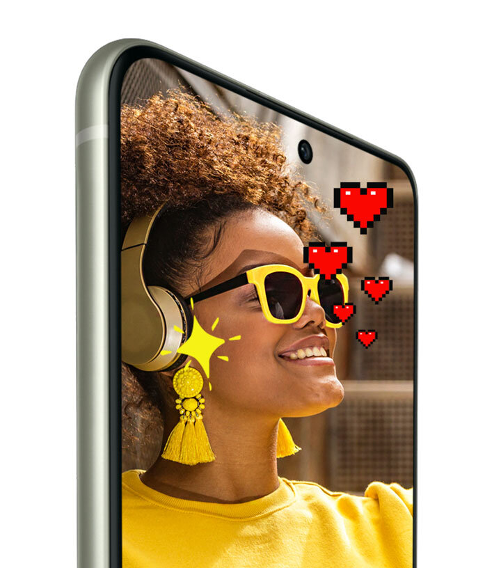 Na ekranie smartfona widoczna jest osoba w żółtych okularach i słuchawkach, z pikselowymi sercami i gwiazdką obok twarzy. Obudowa telefonu ma zaokrąglone krawędzie.