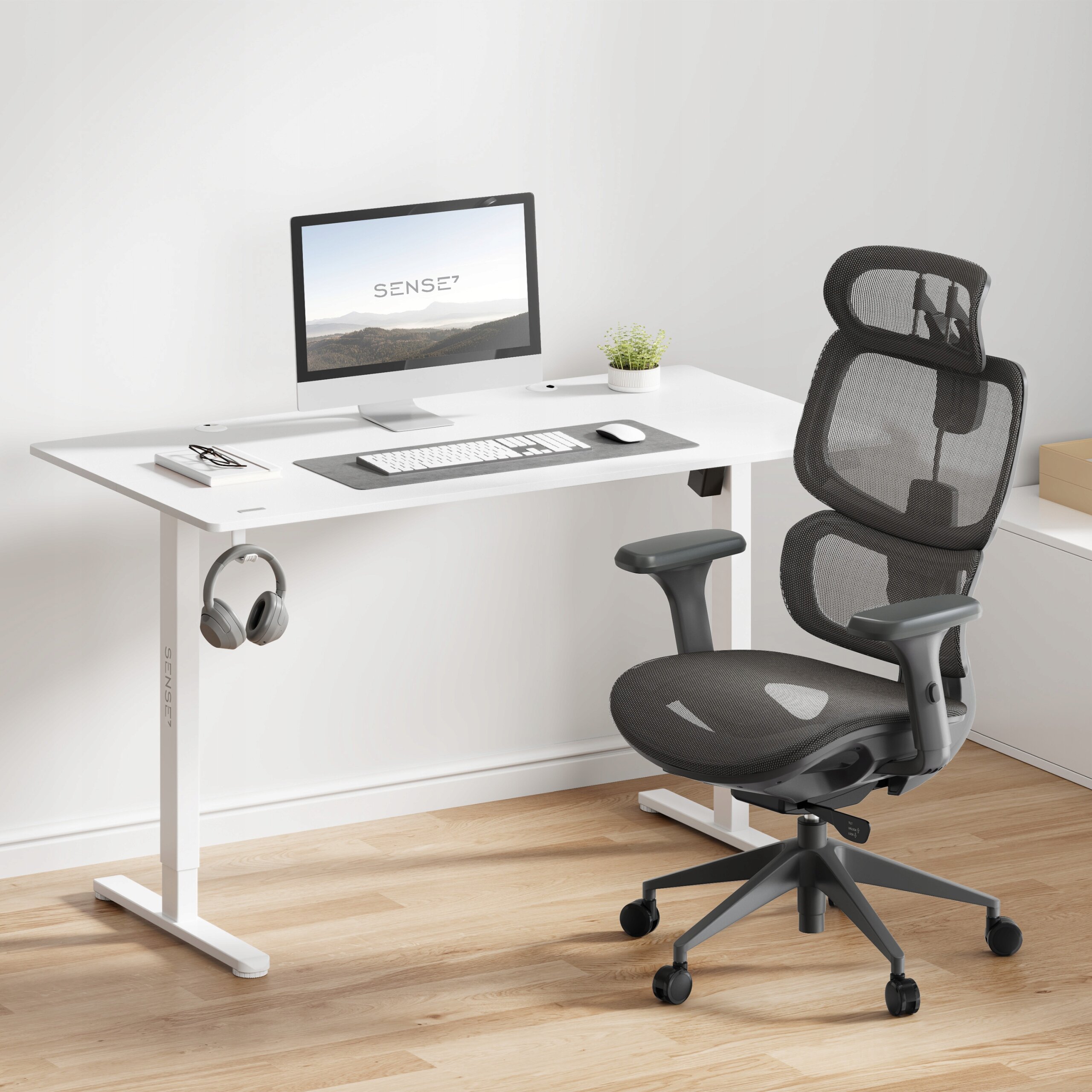 Na obrazie znajduje się biurko z komputerem, na którym widoczny jest napis \'SENSE7\'. Obok biurka stoi ergonomiczne krzesło biurowe w kolorze grafitowym.