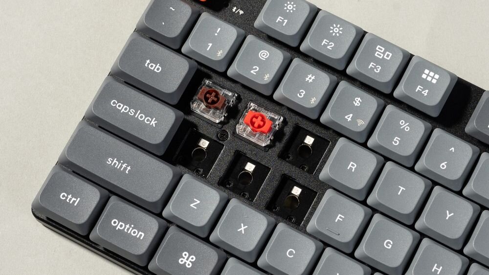Keychron K13 Max niskoprofilowe przełączniki mechaniczne Gateron Low Profile MX 2.0 krótkim skoku szybiej reakcji funkcję hot-swap wymianę przełączników bez lutowania kompatybilna wyłącznie z mechanicznymi przełącznikami low-profile Gateron i Keychron - Zbliżenie na częściowo zdemontowane klawisze klawiatury, odsłaniające brązowy i czerwony przełącznik oraz puste gniazda hot-swap na płytce drukowanej.