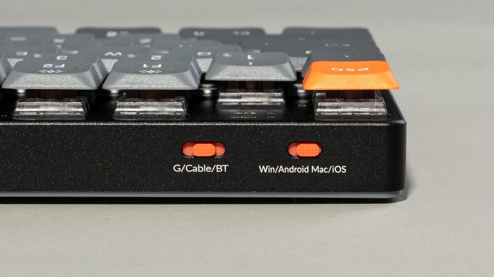 Keychron K13 Max połączenie bezprzewodowe 2.4 GHz częstotliwością odświeżania 1000 Hz Bluetooth 5.1 tryb przewodowy USB-C szybkie przełączanie się między urządzeniami systemami macOS, Windows oraz Linux keycapy systemowe konfiguracja układów klawiszy baterię o pojemności 2000 mAh - Widok na tył klawiatury z dwoma pomarańczowymi przełącznikami suwakowymi do zmiany trybu połączenia oraz systemu operacyjnego.