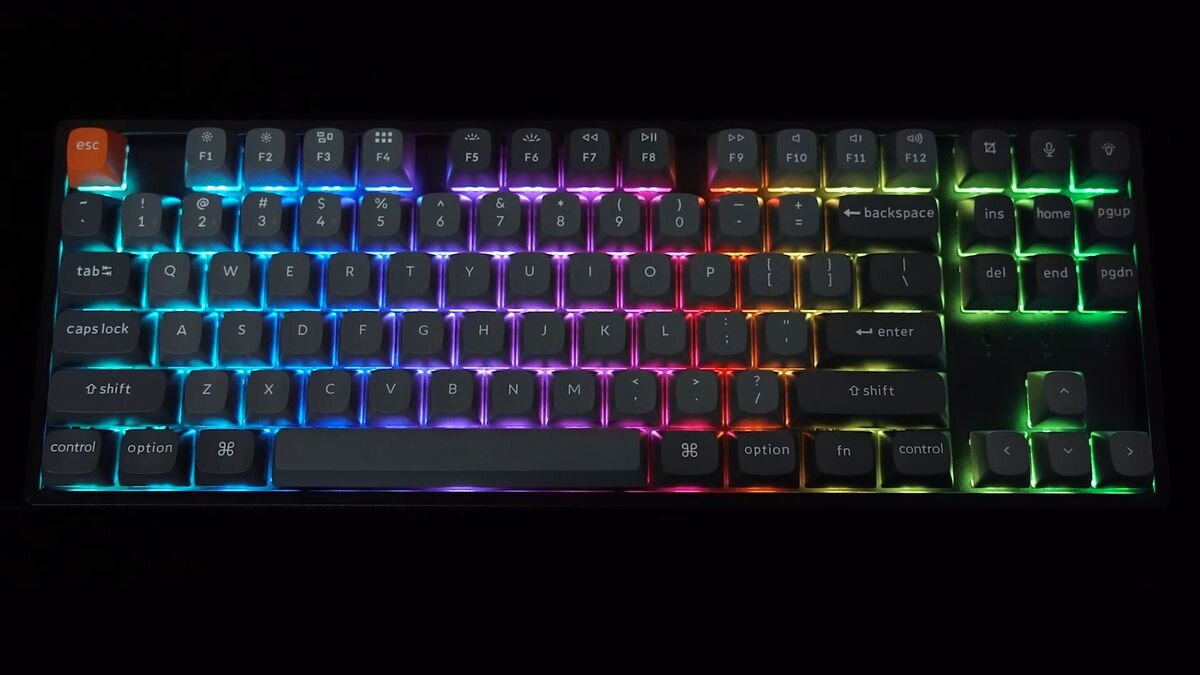 Keychron K8 Max Podświetlenie RGB skierowane na południe pełną kompatybilność z alternatywnymi keycapami o profilu Cherry 22 tryby podświetlenia RGB regulacji odcienia, nasycenia, jasności i szybkości efektów - Klawiatura z włączonym podświetleniem klawiszy zaprezentowana na ciemnym tle.