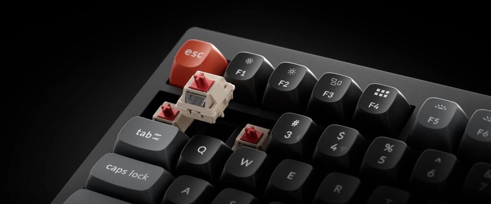 Czarna klawiatura z czerwonym klawiszem \'esc\' i widocznymi czerwonymi przełącznikami mechanicznymi. Klawisze mają oznaczenia takie jak \'tab\', \'caps lock\', \'F1\', \'F2\', \'F3\', \'F4\', \'F5\'.