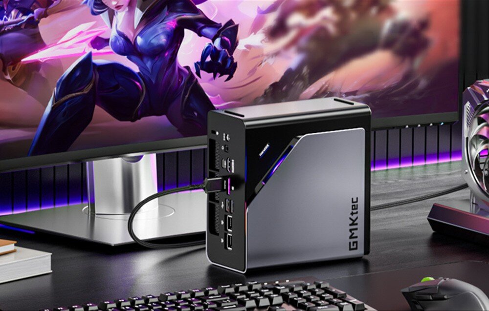 Komputer GMKTEC K15-32RAM Mini PC GMKtec K15 stoi na biurku obok monitora wyświetlającego dynamiczną grafikę z gry komputerowej, opis