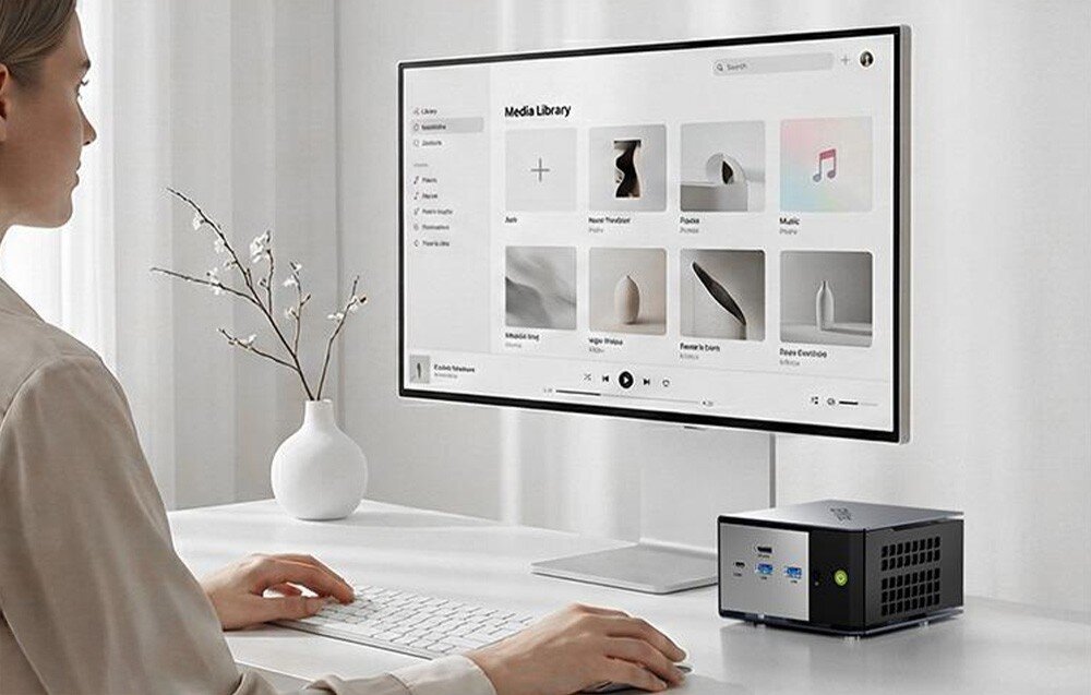 Komputer GMKTEC K16 Kobieta pracuje przy biurku, korzystając z monitora wyświetlającego bibliotekę mediów oraz kompaktowego Mini PC GMKtec K6, opis