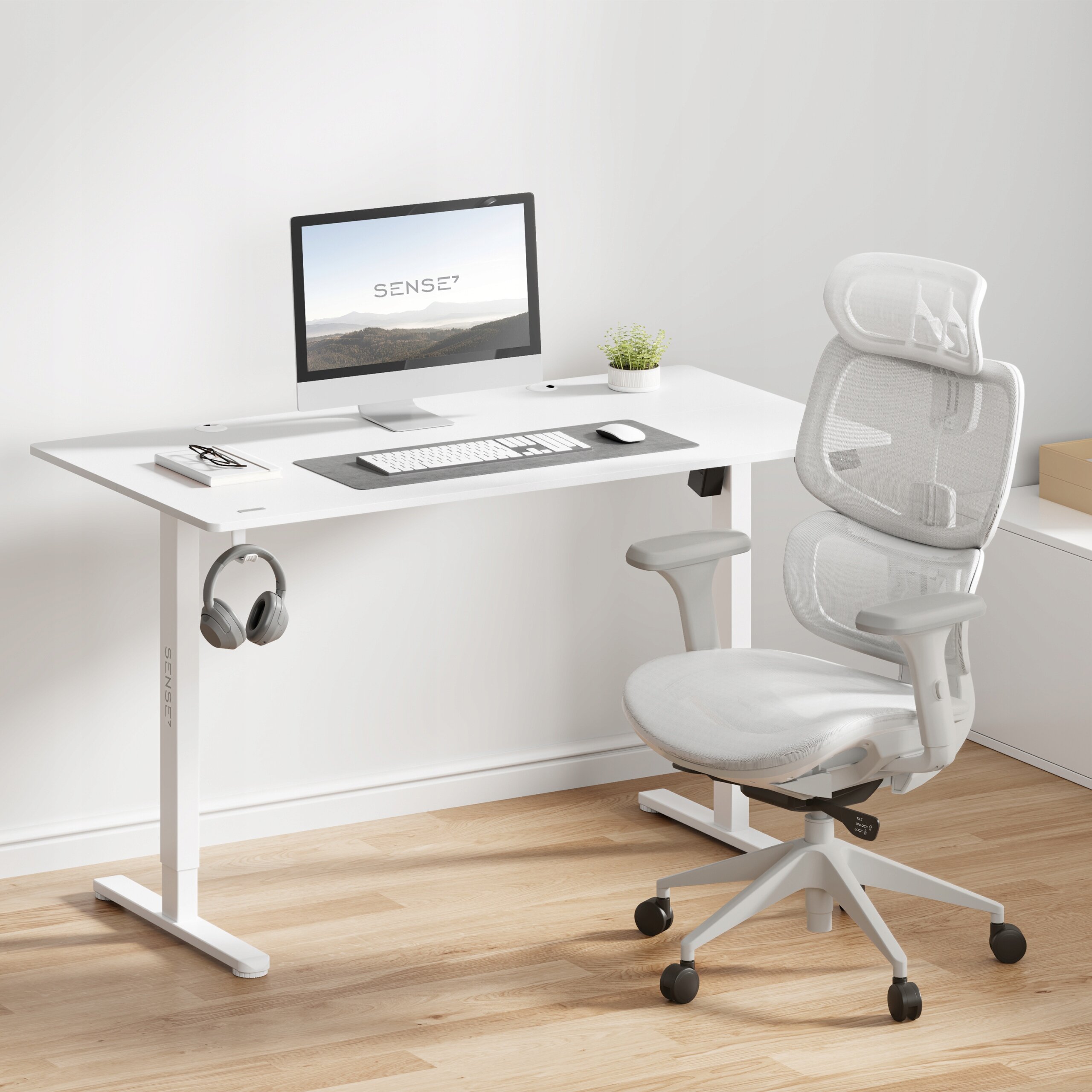 Na obrazie znajduje się biurko z komputerem, klawiaturą i myszką, a obok stoi jasno-szary, ergonomiczny fotel biurowy. Na ekranie komputera widoczny jest napis \'SENSE7\'.