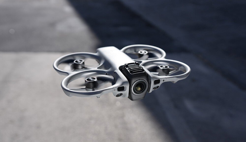 Na zdjęciu widać drona z czterema śmigłami i wbudowaną osłoną śmigieł, unoszącego się w powietrzu. Dron ma kompaktową, aerodynamiczną konstrukcję i jest widoczny na tle rozmytego krajobrazu.