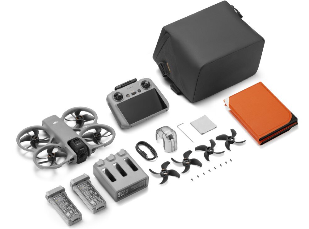 Na obrazie widoczny jest zestaw drona z akcesoriami, w tym kontroler, baterie, ładowarka, śmigła, torba i inne elementy. Dron ma wbudowaną osłonę śmigieł i jest w kolorze szarym.